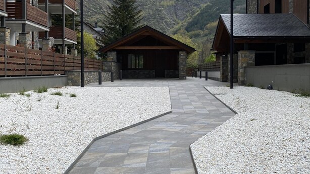 A modern building with a stone facade, a wooden deck, and a stone pathway leading to a wooden cabin.