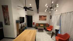 Un soggiorno moderno con un tavolo da pranzo in legno, un divano verde, sedie rosse, una ventola a soffitto e un lampadario originale.