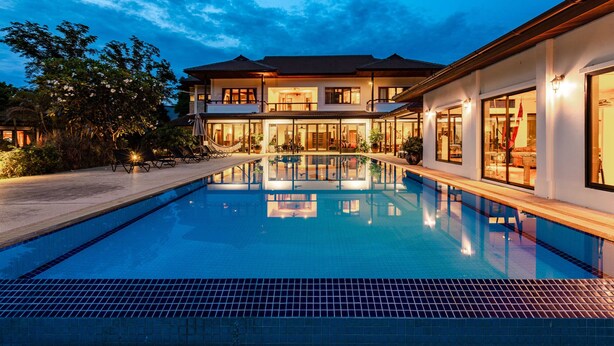 Una casa moderna de dos pisos con piscina, ventanas amplias e iluminación exterior.