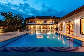 Una casa moderna de dos pisos con piscina, ventanas amplias e iluminación exterior.
