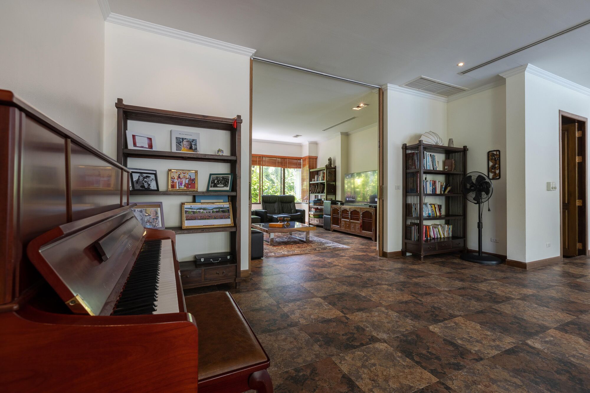 Un salón amplio con un piano, una estantería y un ventilador de techo grande.
