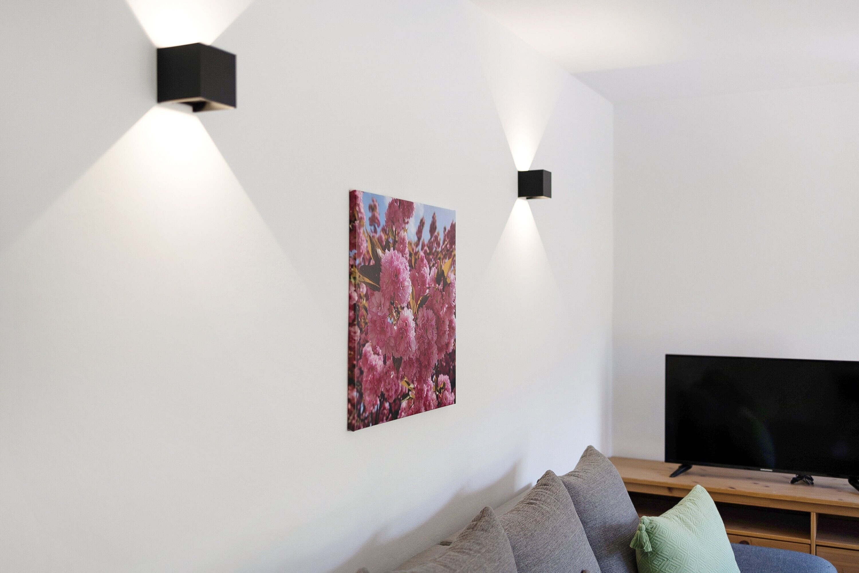 Ein modernes Wohnzimmer mit Flachbildfernseher, einer Couch und zwei Wandleuchten.