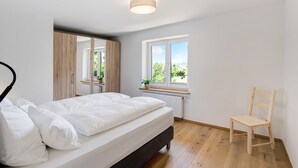 Un dormitorio con una cama, una silla de madera, una ventana con vistas y una lámpara en el techo.