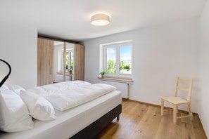 Ein Schlafzimmer mit Bett, einem Holzbstuhl, einem Fenster mit Blick und einer Deckenleuchte.