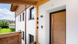 Un edificio moderno con puerta de madera, un balcón y vista a un paisaje verde.
