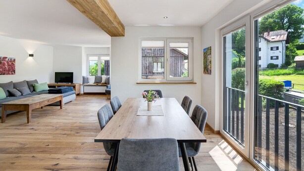 Amplia sala de estar con una mesa de comedor de madera, sillas tapizadas de gris, un sofá y una televisión.