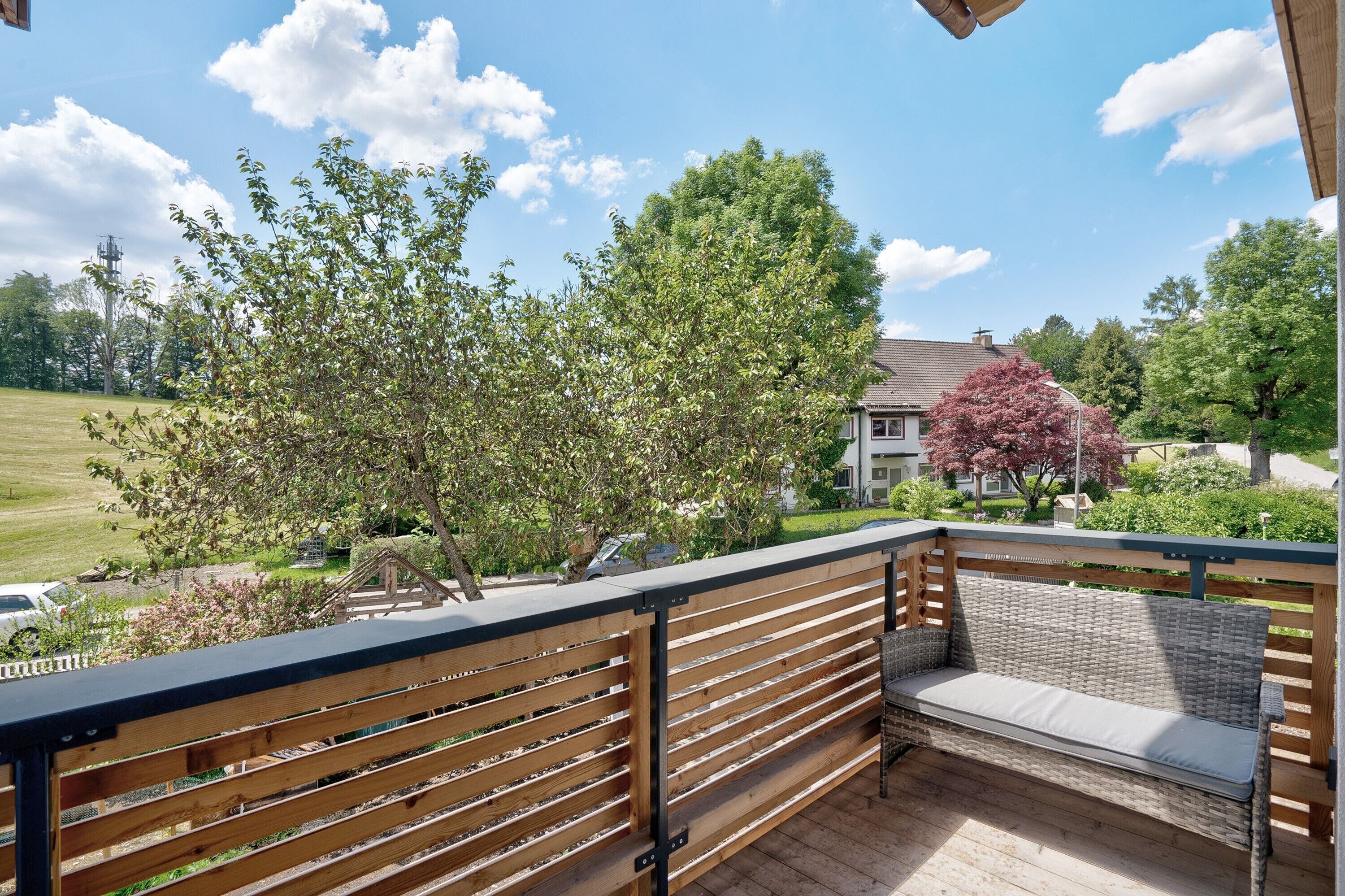 Eine Holzterrasse mit einer Bank und einem Geländer, mit Blick auf eine grüne Rasenfläche und Bäume.