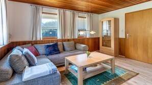 A cozy living room with a wooden ceiling, a sofa with cushions, a coffee table, and a cabinet with glass doors.