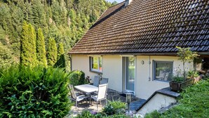 A house with a tiled roof, a patio with a table and chairs, and a garden with various plants.