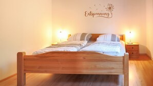 A wooden bed with a white and gray striped blanket, two bedside lamps, and a wall with a dandelion illustration and the word 'Entspannung'.