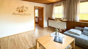 A room with a wooden ceiling, a sofa, a table with a vase and a book, and a wall with a mountain illustration and text.