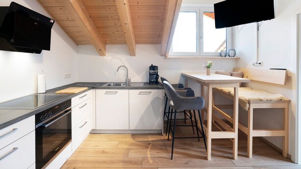 Een moderne keuken met een zwart fornuis, witte kasten en een houten plafond.