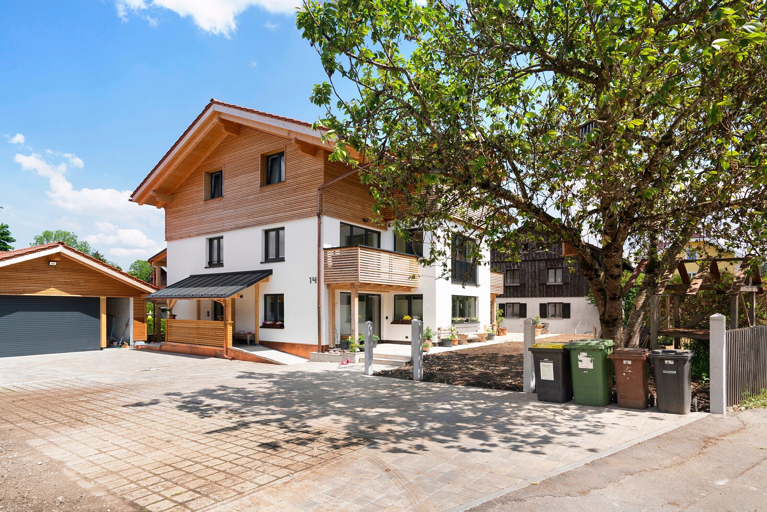 Ein zweistöckiges Haus mit Garage, einer Veranda und einem Baum im Vorgarten.