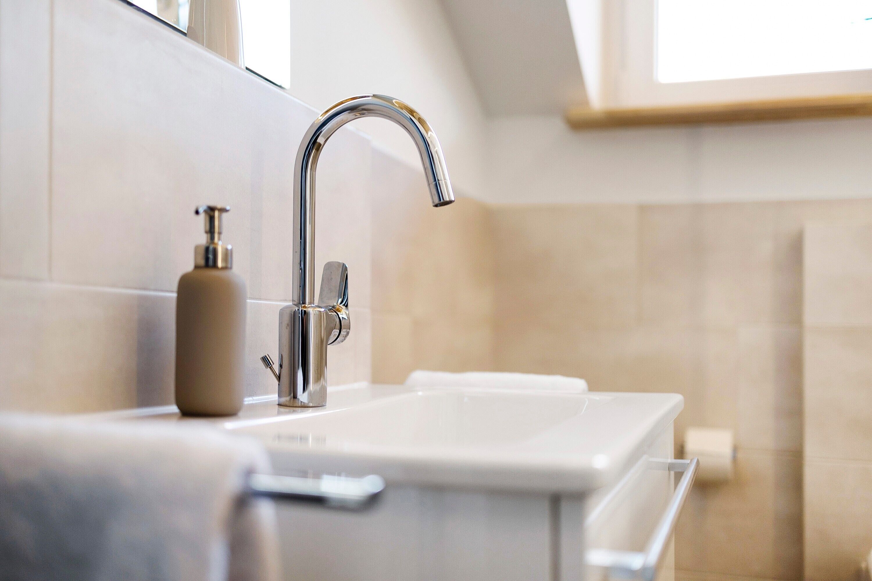 Une salle de bain avec un lavabo moderne, un distributeur de savon et une fenêtre au-dessus du lavabo.