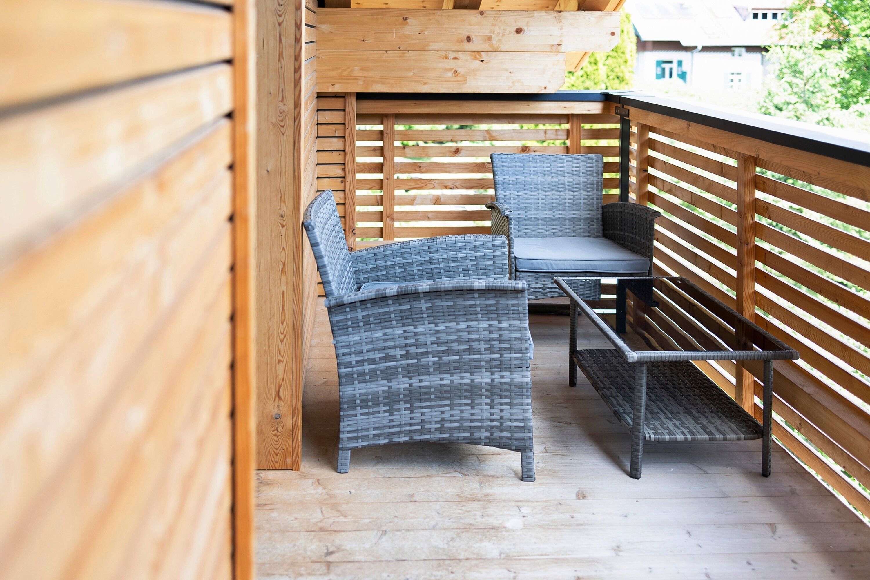 A wooden deck with wicker furniture, including a bench and two chairs.