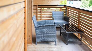 A wooden deck with wicker furniture, including a bench and two chairs.