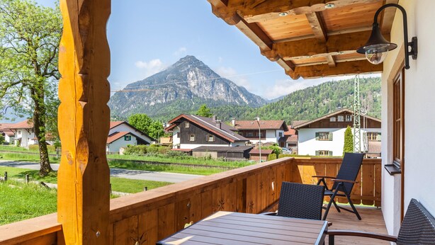 Una terraza de madera con una mesa y sillas, con vistas a una montaña y casas.