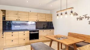 Una cocina moderna con armarios de madera, horno empotrado y comedor con banco y mesa.