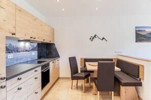 Une cuisine moderne avec des meubles en bois, une cuisinière encastrée et un coin repas comprenant une banquette et des chaises.