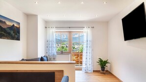 A modern room with a wooden table, a sofa, a TV mounted on the wall, and a window with curtains. - Apartment 'Ferienwohnung Vrenal' with Mountain View, Shared Garden and Wi-Fi (Farchant)