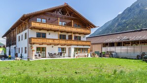 A multi-story building with wooden balconies, a front porch with seating, and a mountain backdrop. - Apartment 'Ferienwohnung Vrenal' with Mountain View, Shared Garden and Wi-Fi (Farchant)