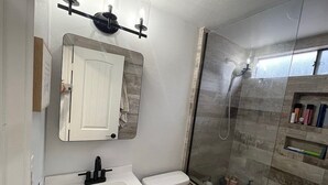 Un baño con lavamanos blanco, inodoro, espejo y ducha con mampara de vidrio.