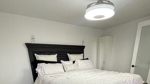 Un dormitorio con estructura de cama de madera oscura, ropa de cama blanca y una lámpara en el techo.