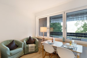 A room with a dining table, two chairs, a lamp, and a view through large windows. - Holiday Apartment "in Ruhiger Aussichtslage" with Balcony & Wi-Fi (Bad Liebenzell)