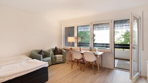 Une pièce comprenant un lit, un canapé vert, une table à manger avec des chaises et une porte-fenêtre coulissante donnant sur un balcon extérieur.