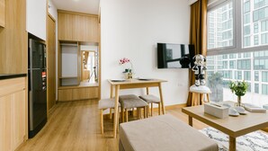 A modern kitchen with wooden cabinets, a built-in refrigerator, a dining area with a table and chairs, a small bench, and a TV mounted on the wall. - The Euphoria Hanoi (Hanoi)