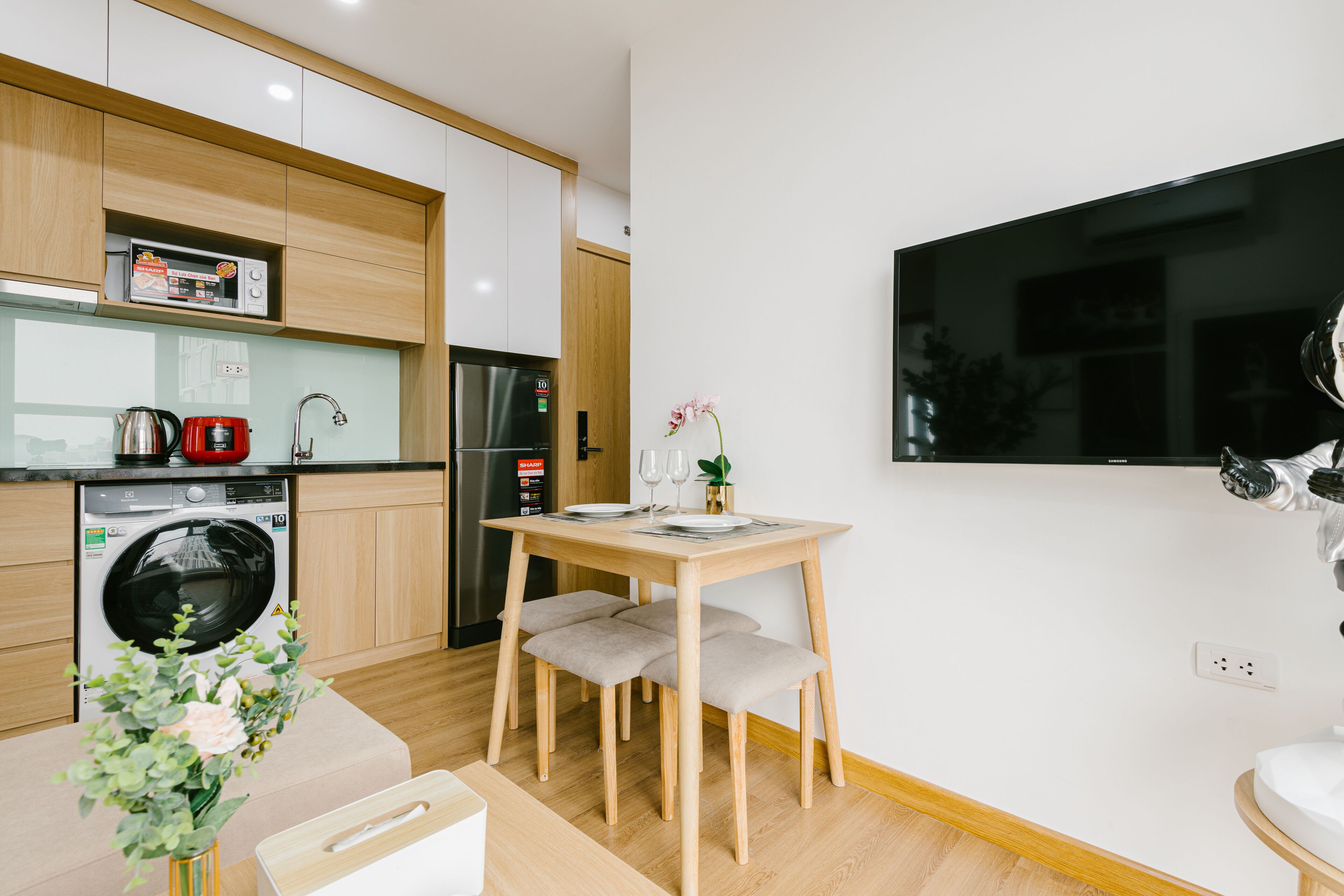 A modern kitchen with a built-in oven, microwave, and dishwasher. There is a dining table with chairs and a vase of flowers.
