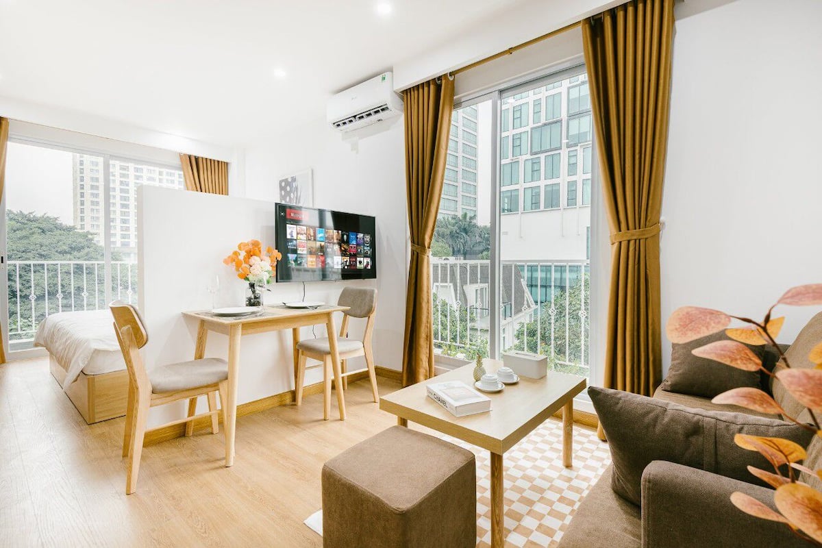 Ein modernes Wohnzimmer mit Sofa, Esstisch mit Stühlen, Fernseher und einem Balkon mit Vorhängen.