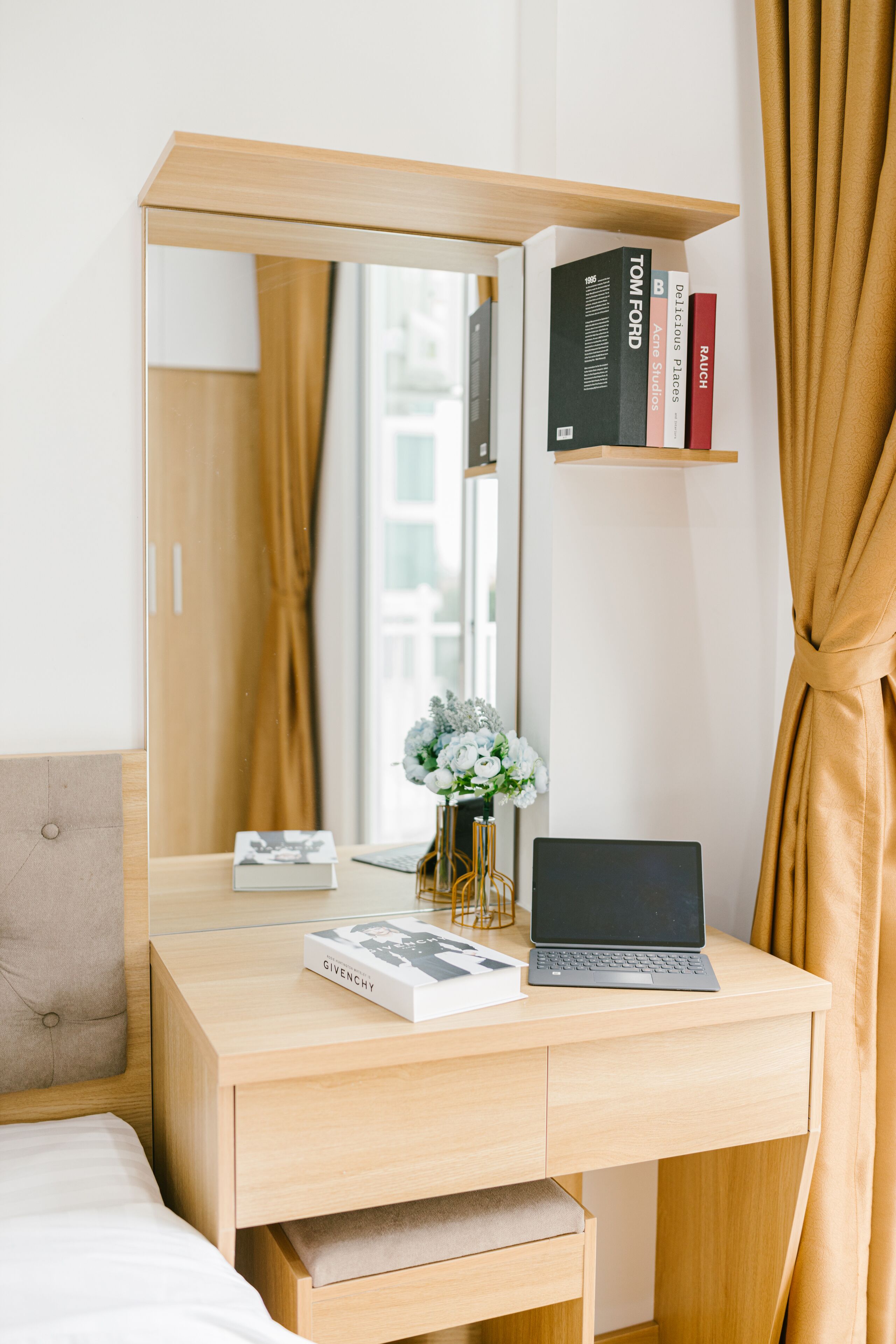 A modern bedroom with a wooden desk, a laptop, a book, and a mirror.