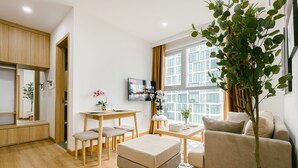 A modern living room with a sofa, a dining table with chairs, a TV, and a large window with curtains. - The Euphoria Hanoi (Hanoi)