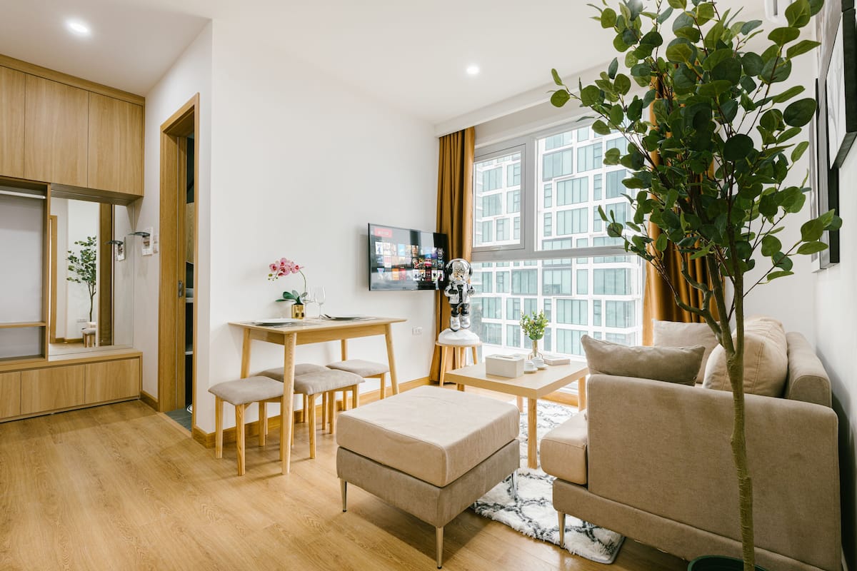 Ein modernes Wohnzimmer mit einer Couch, einem Esstisch mit Stühlen, einem Fernseher und einem großen Fenster mit Vorhängen.