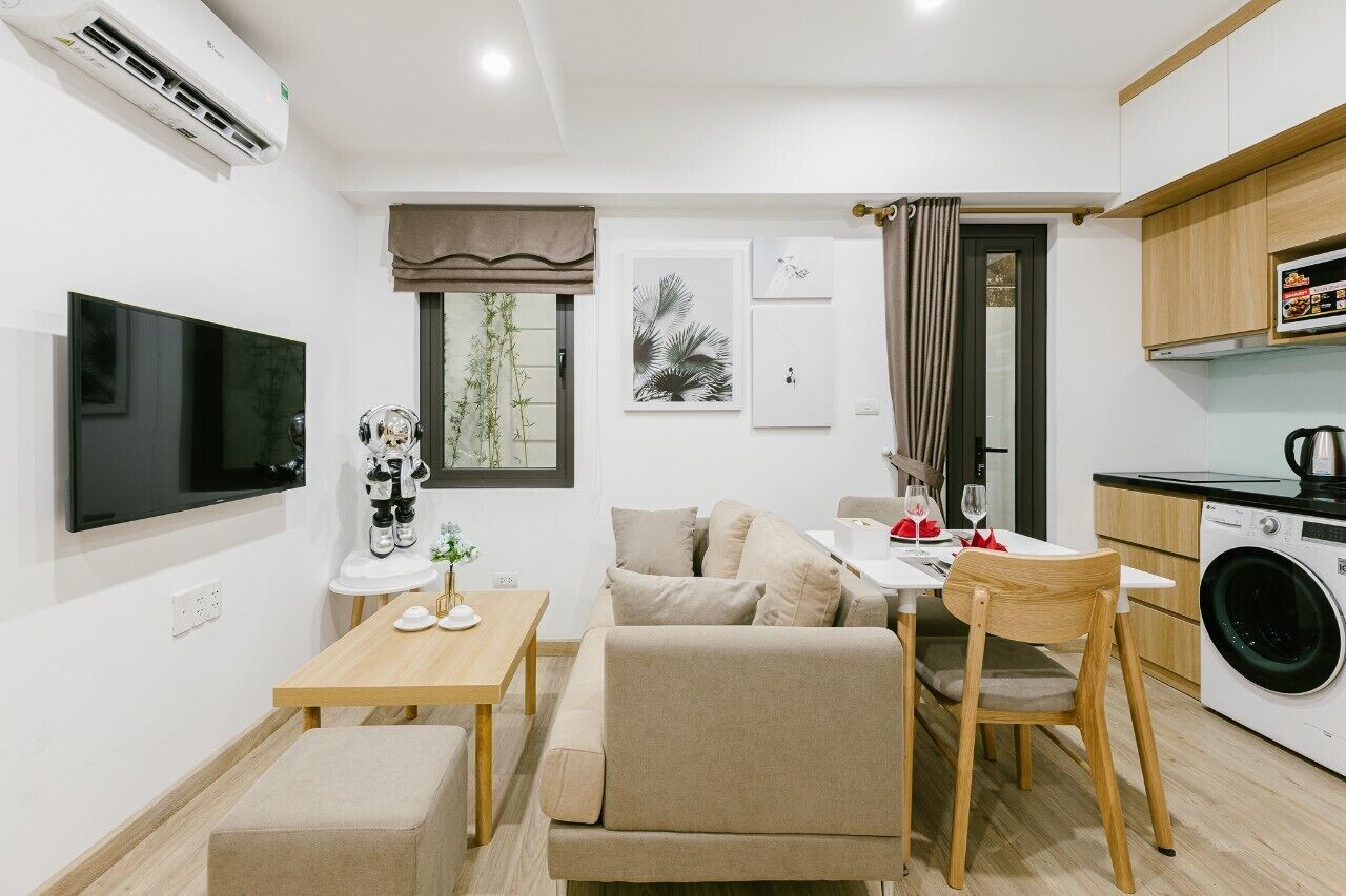 A compact living space with a flat-screen TV, a sofa, a dining table, a washing machine, and a small statue.