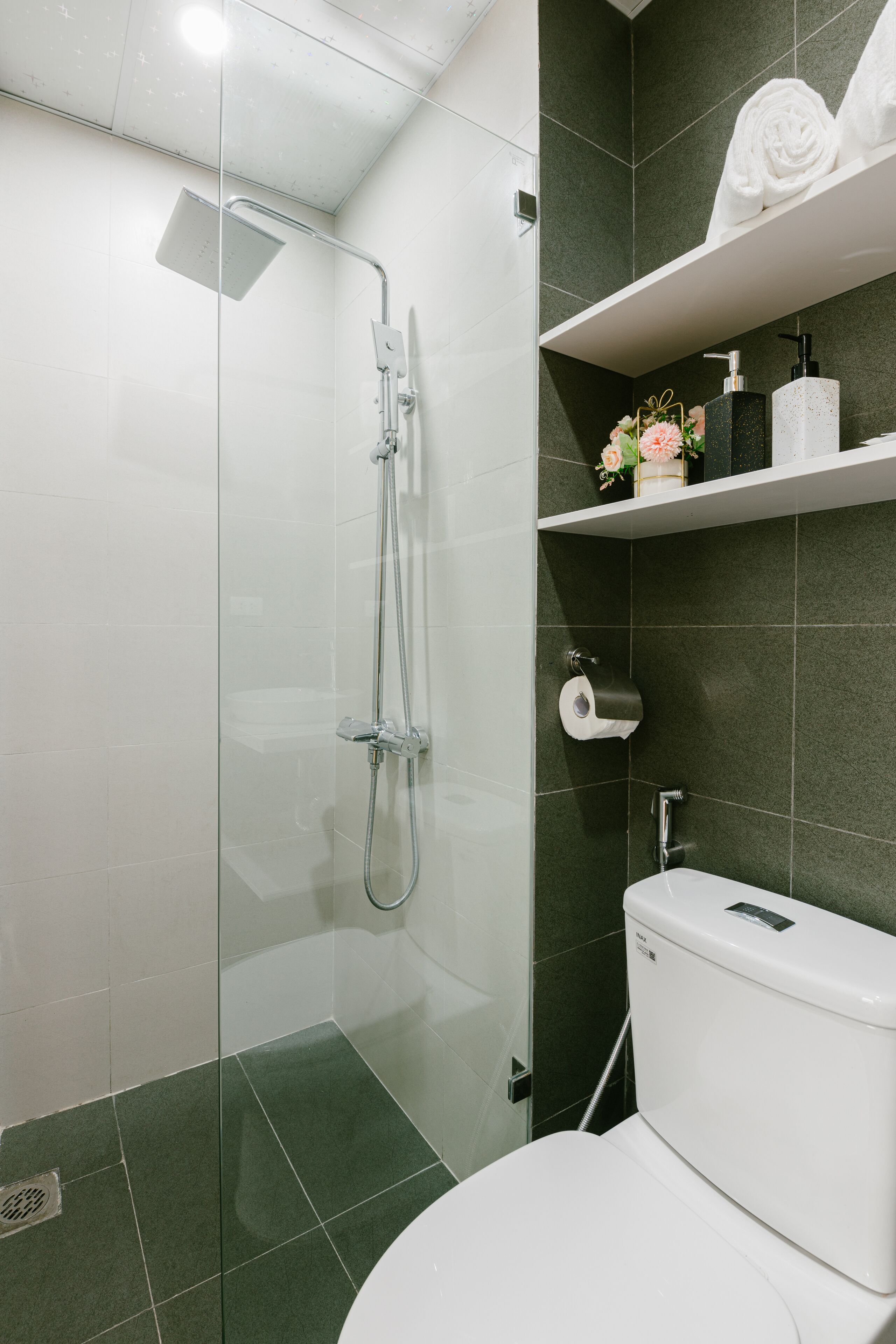 A modern bathroom with a glass-enclosed shower, a toilet, and a shelf with toiletries.