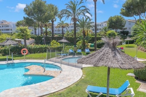 Une piscine entourée d’une terrasse en pierre, de pelouse et de palmiers, avec des chaises longues et des parasols.