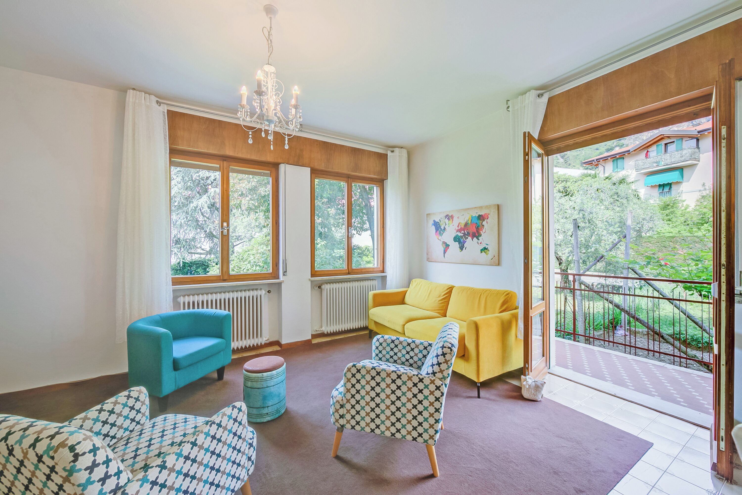 A living room with a blue armchair, a patterned armchair, a yellow sofa, and a chandelier.