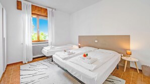 Habitación de hotel con dos camas, un radiador, una ventana con cortinas, una mesita con lámpara y una alfombra estampada.
