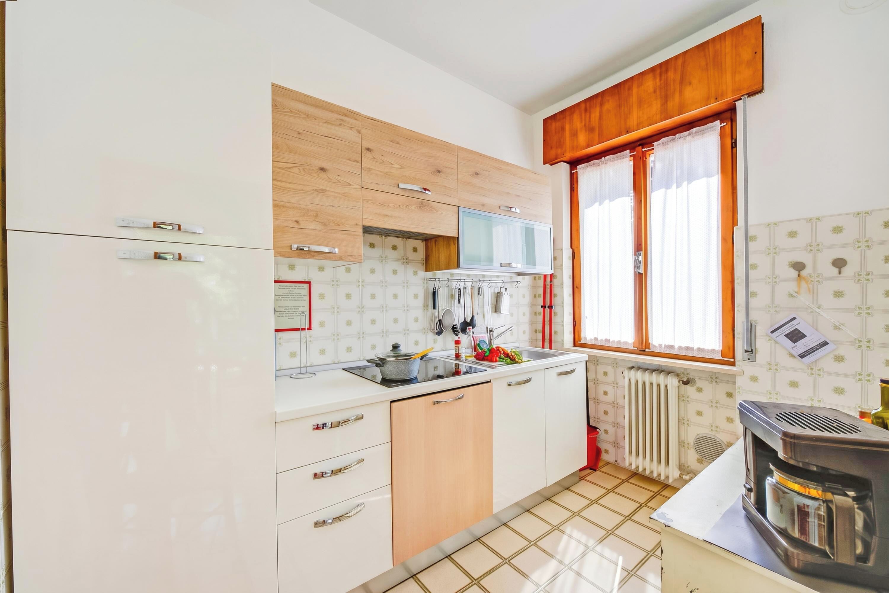 A kitchen with white cabinets, a microwave, a stove, and a window with curtains.