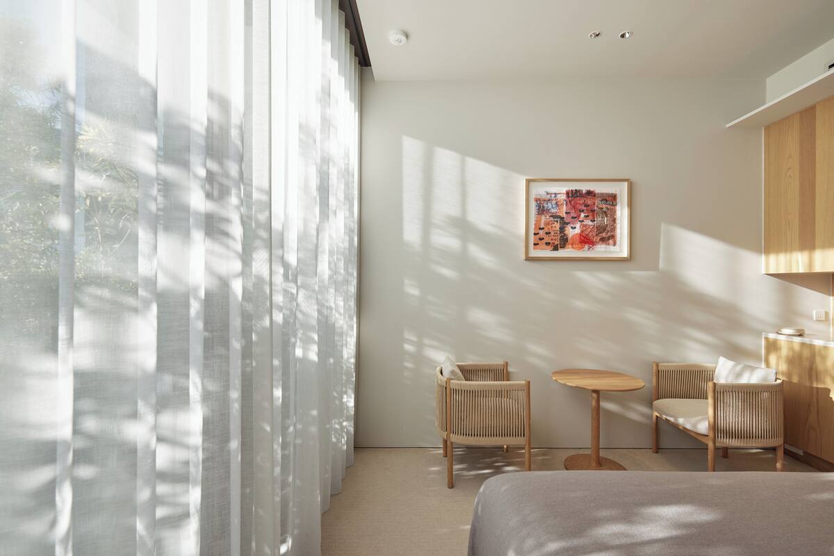 A modern hotel room with a bed, two chairs, a small table, and a painting on the wall.