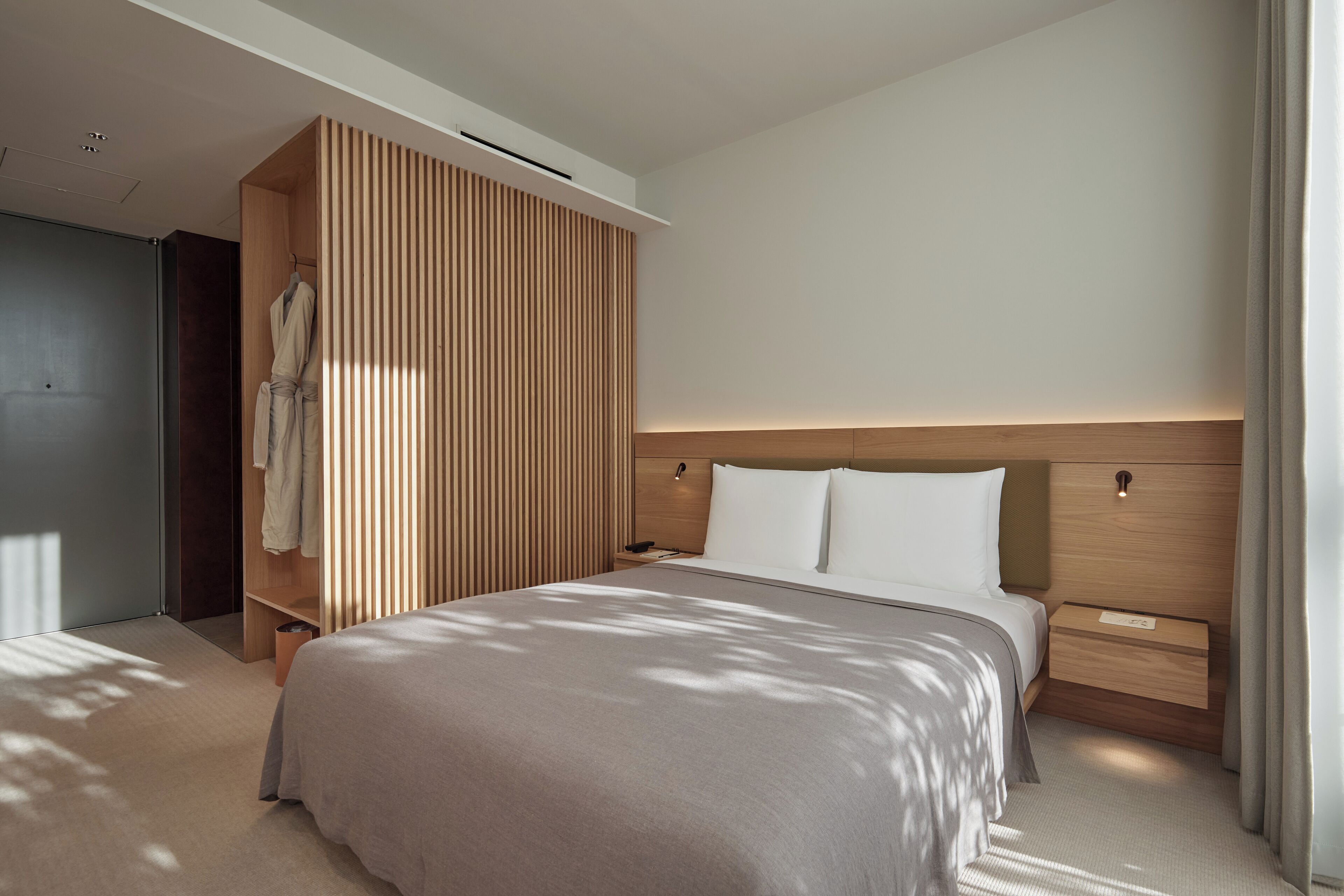 A modern hotel room with a large bed, a wooden wardrobe, a bedside table, and a nightstand.