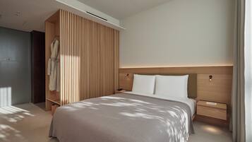 A modern hotel room with a large bed, a wooden wardrobe, a bedside table, and a nightstand.