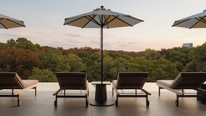A terrace with three lounge chairs and a central umbrella, overlooking a forested hillside. - TRUNK HOTEL YOYOGI PARK (Tokyo)