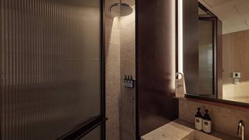 A modern bathroom with a shower, a large mirror, and a vanity with two bottles of shampoo.