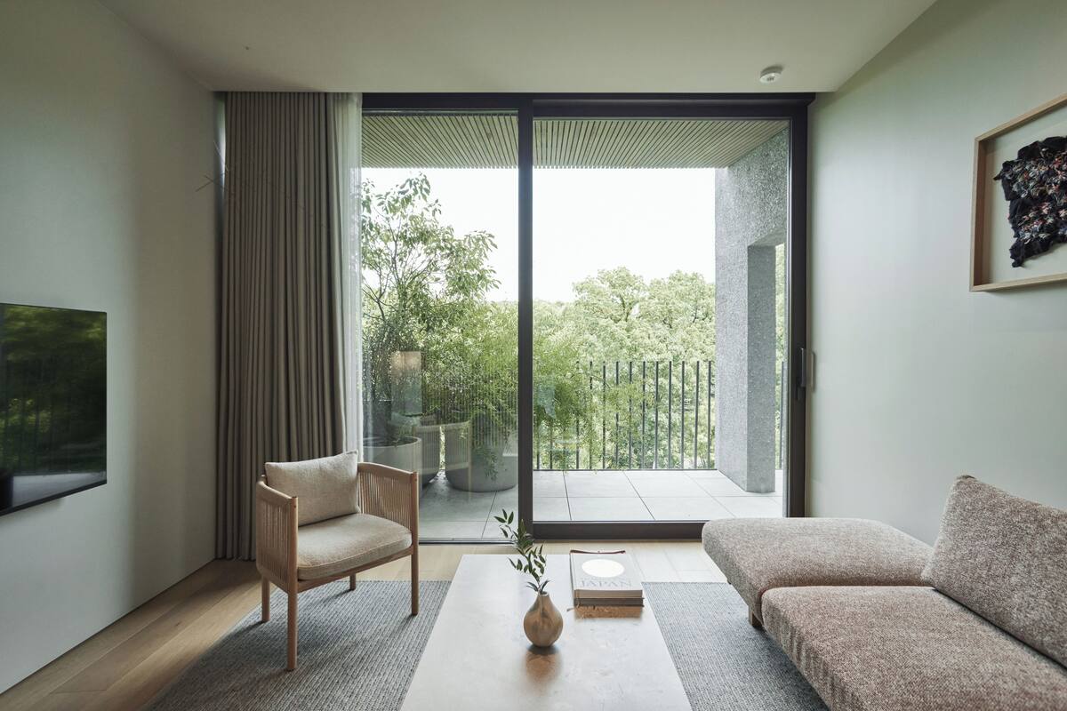 A modern living room with a sofa, a chair, a coffee table, and a large window offering a view of greenery outside.