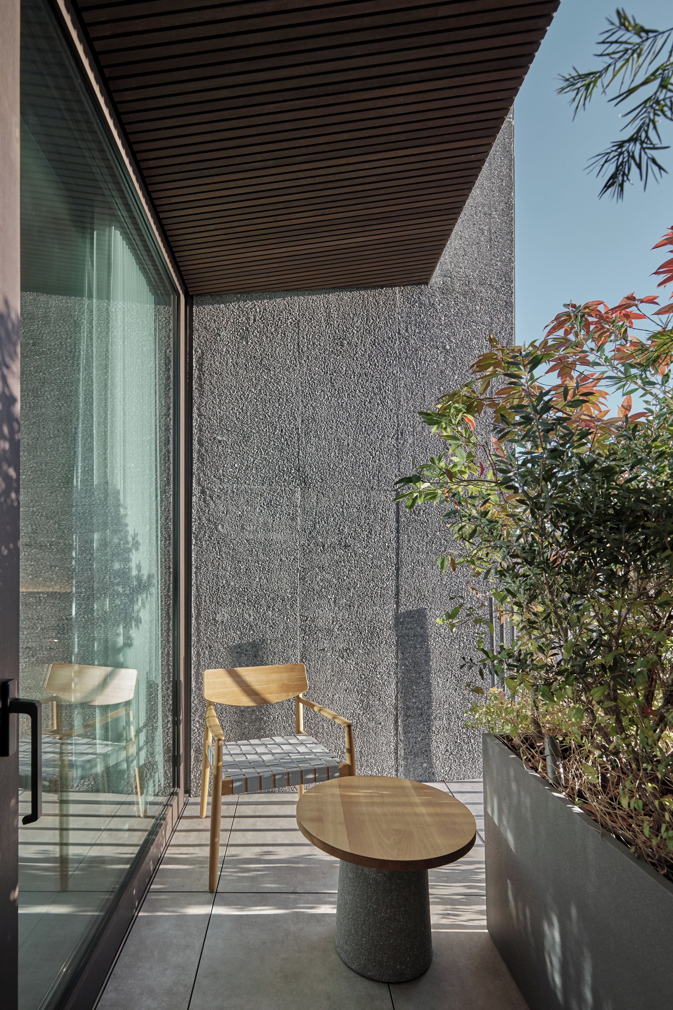 A modern outdoor seating area with a round table and chairs, a glass partition, and a textured wall.