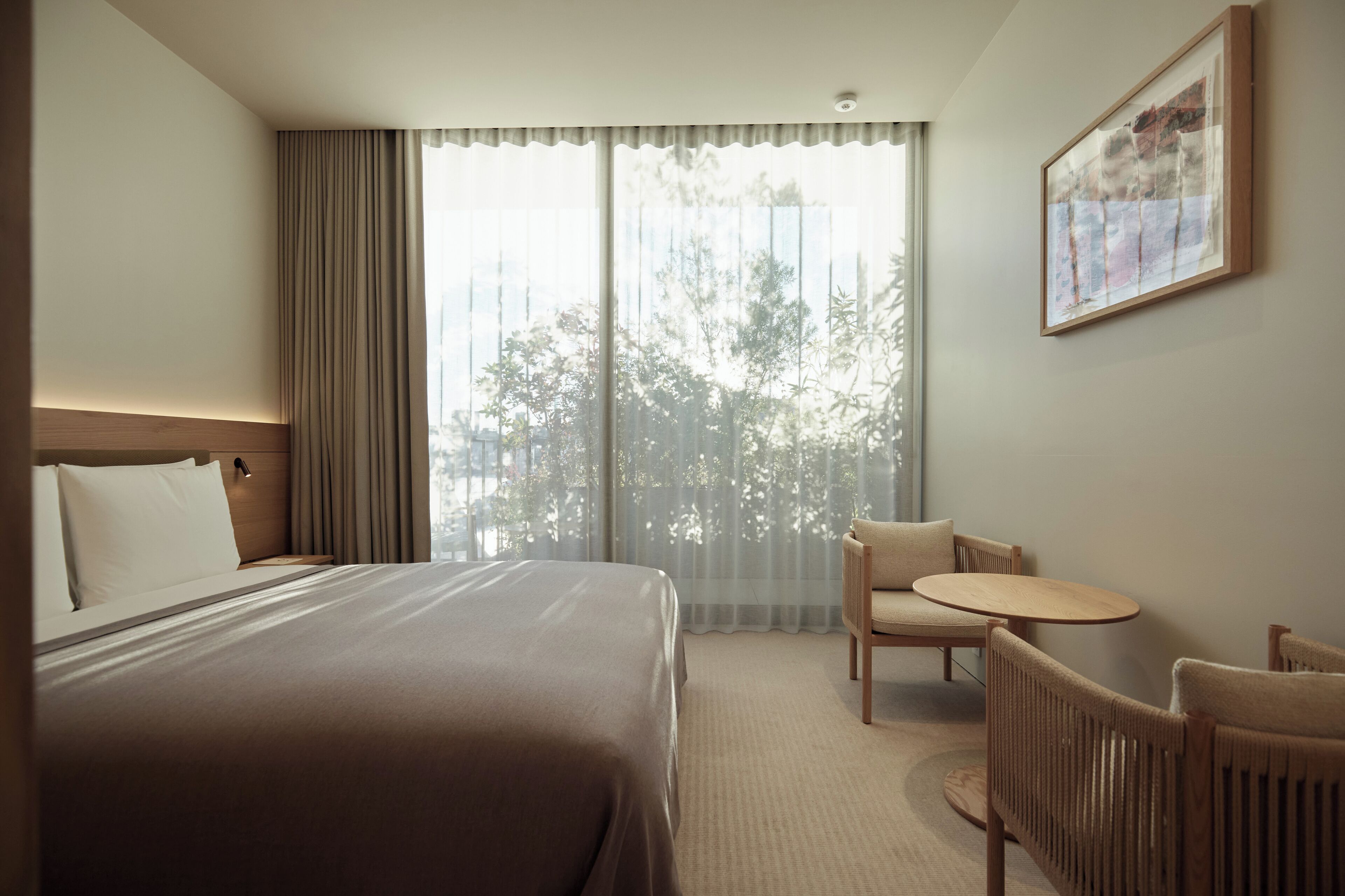 A hotel room with a large bed, a small round table, two chairs, a window with curtains, and a framed picture on the wall.