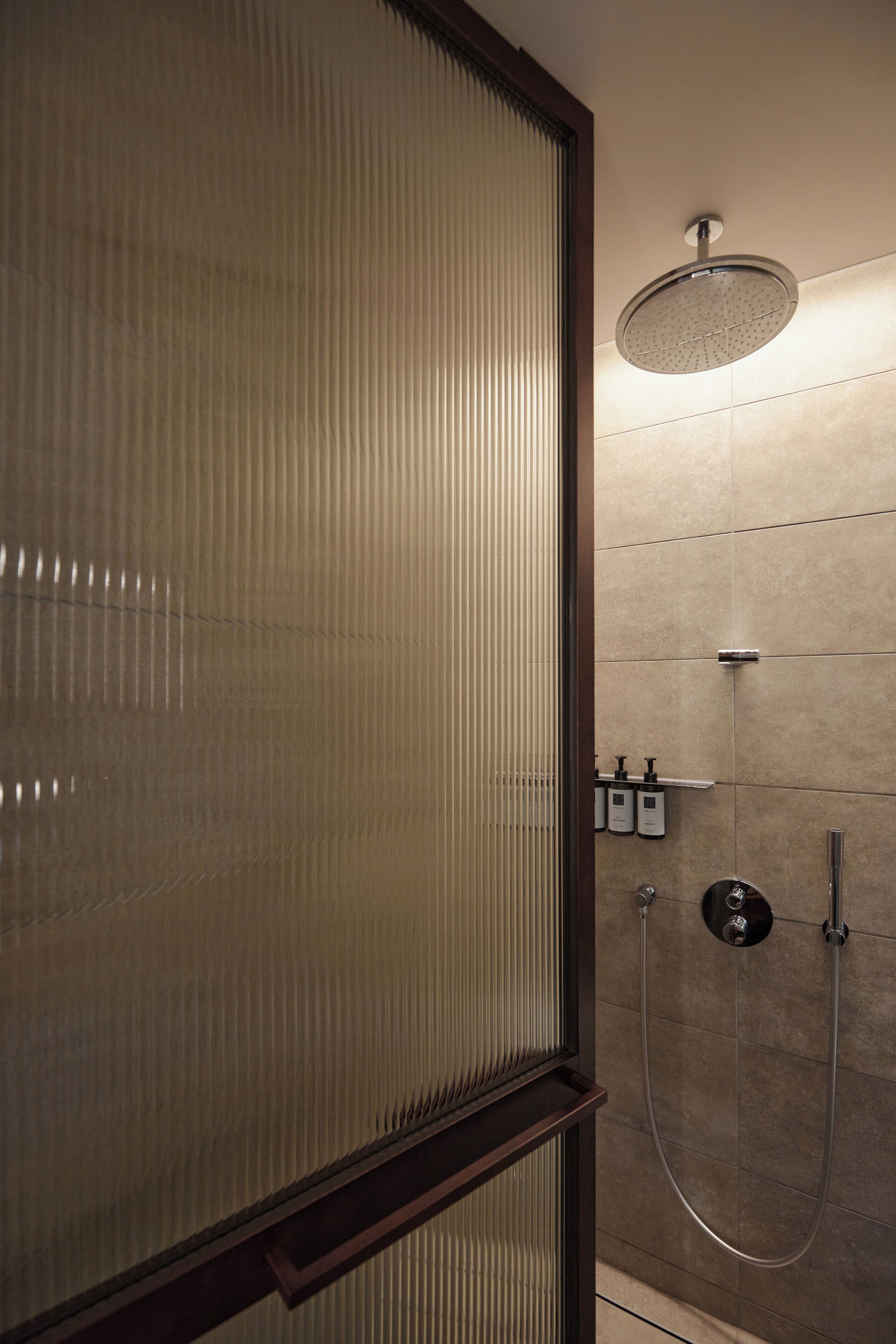 A modern bathroom with a glass partition, a round showerhead, and a wall-mounted faucet.